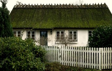 Landhus med stråtag og hvidt stakit.