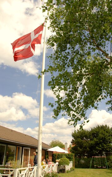 Hvid flagstand i baghave med dannebrog hejst til tops