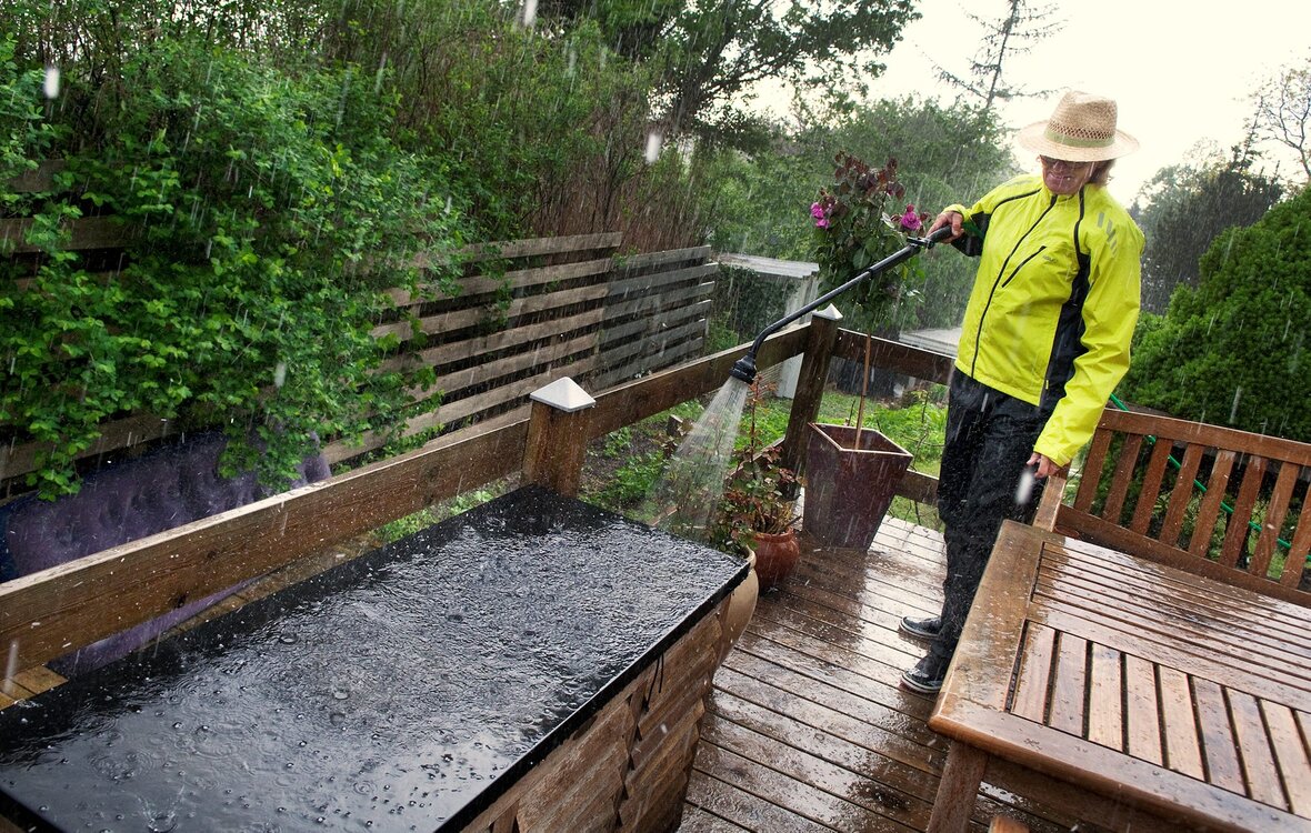 Det kan af og til betale sig at vande haven i regnvejr Kvinder vander potteplanter på terrasse i silende regnvejr