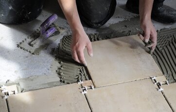 Kvadratiske fliser lægges på et betongulv i badeværelse