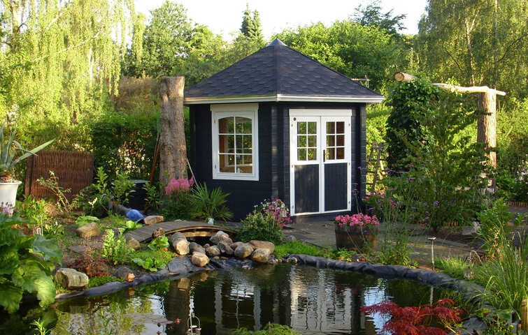 Pavillon af sortmalet træ foran havedam