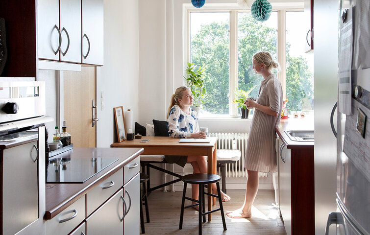 To veninder, der bor sammen som roommates, snakker sammen i køkkenet i lejelejlighed.