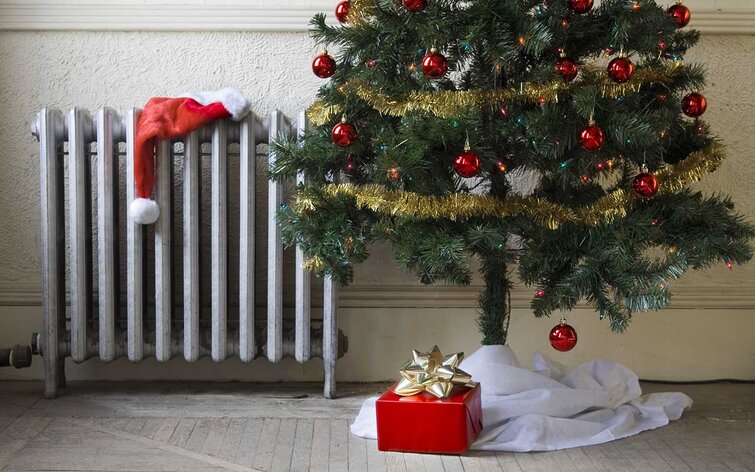 spare skrue ned for varmen juleferie Radiator med nissehue på og juletræ ved siden af
