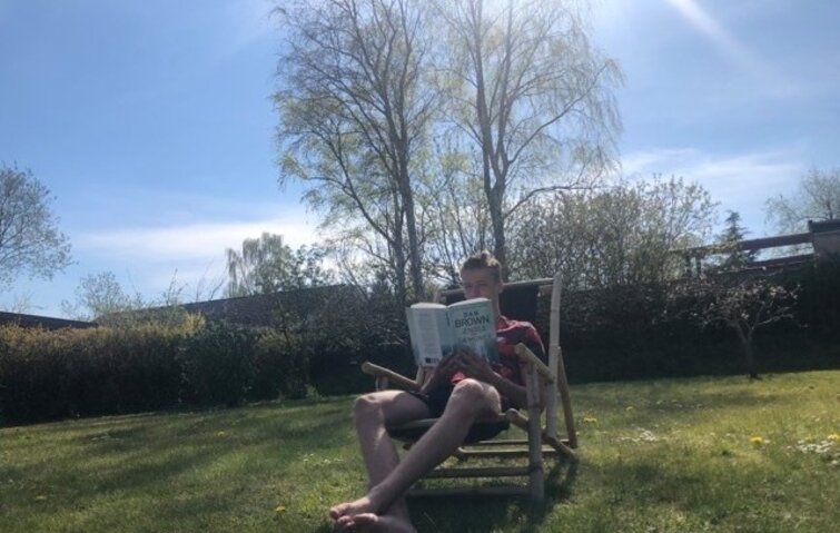 ung mand sidder i skygge i haven og læser da naboens høje træet kaster skygge i haven