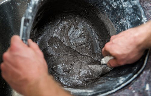 Mørk fugemasse blandes op i sort spand